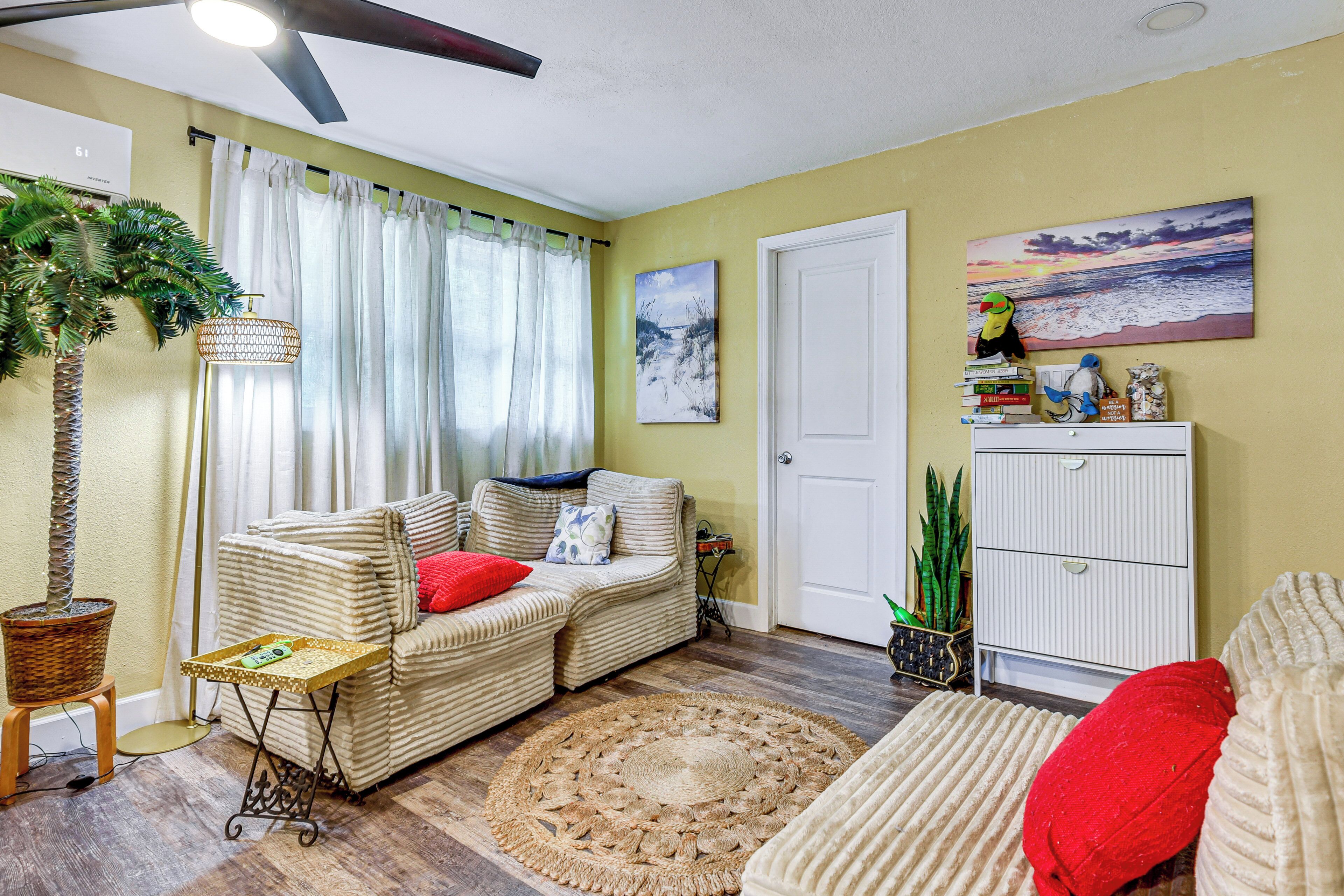 A living room with a sofa, a small table, a floor lamp, a potted plant, and a painting on the wall.