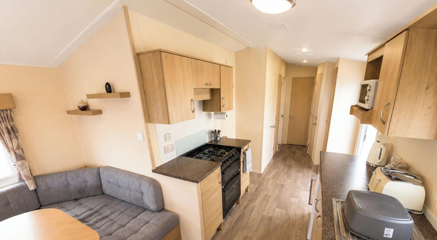 Eine kompakte Küche mit Herd, Backofen und Mikrowelle, ein kleiner Essbereich mit Tisch und einer Couch, sowie Holzschränke.