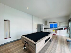 Una habitación moderna con mesa de billar, zona de cocina y vista al mar.