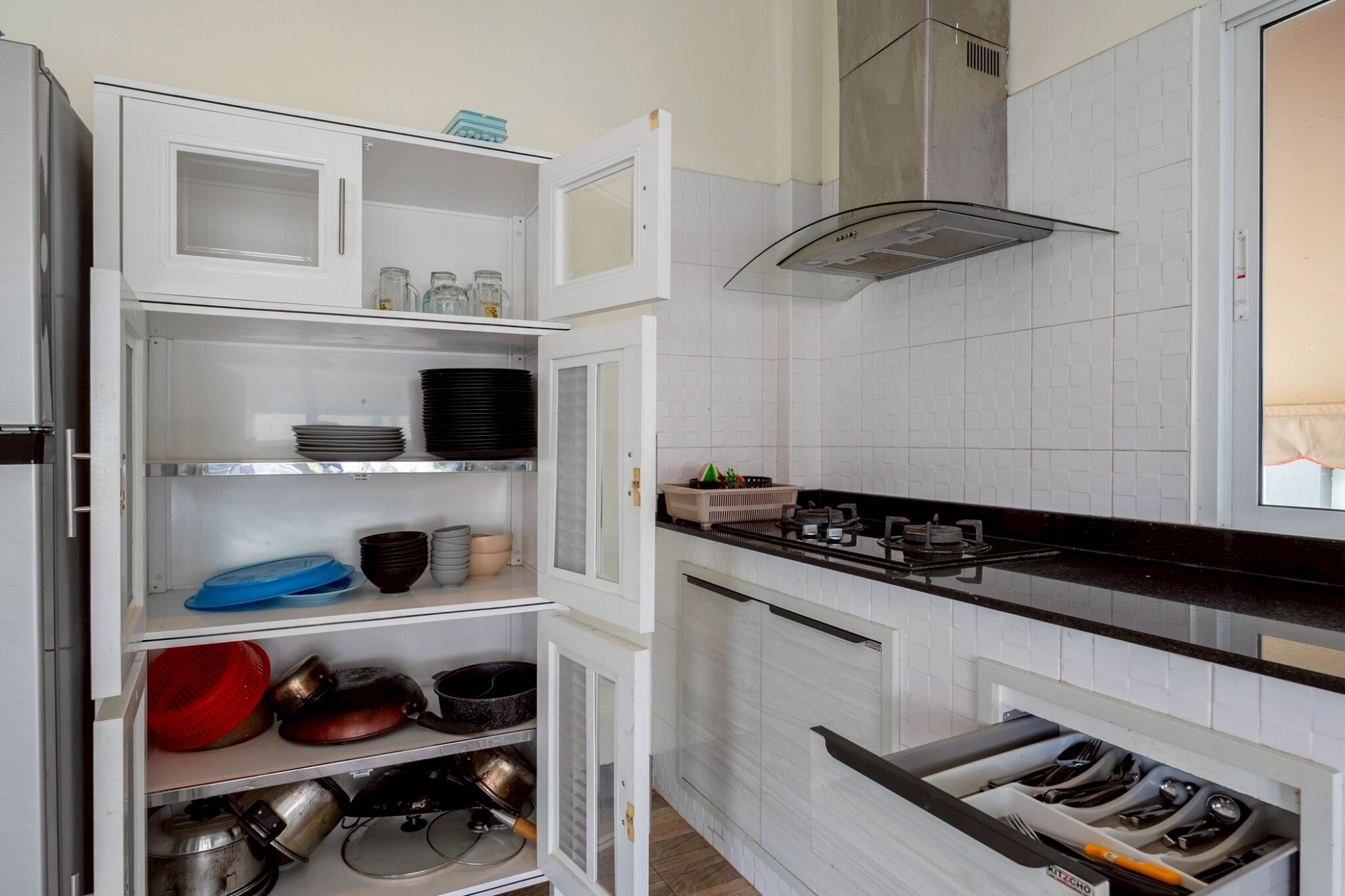 A kitchen with open cabinets, a stove, and a drawer with utensils.