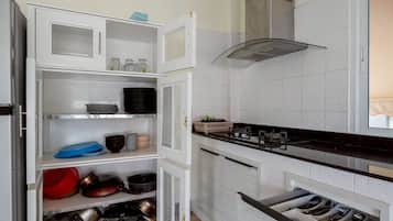 A kitchen with open cabinets, a stove, and a drawer with utensils.