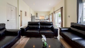 Un salón con sofás de cuero negro, una mesa de centro y vistas a una cocina y zona exterior.