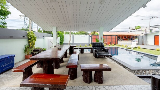 Un patio al aire libre con mesas y bancos de madera, una piscina y una zona de estar cubierta.