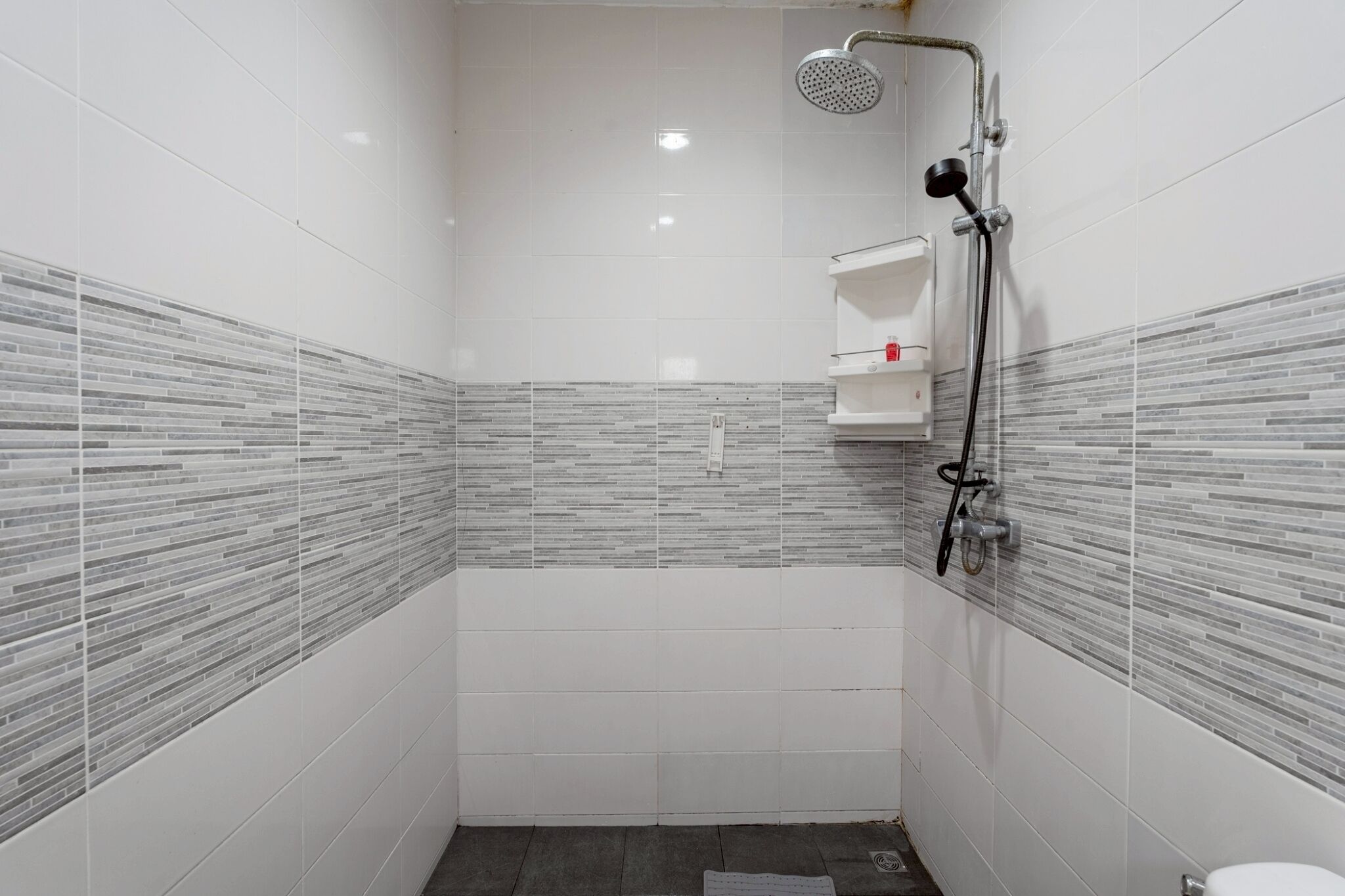 A small, tiled shower room with a handheld showerhead and a wall-mounted faucet.