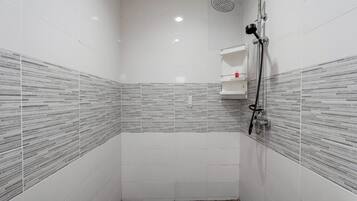 A small, tiled shower room with a handheld showerhead and a wall-mounted faucet.