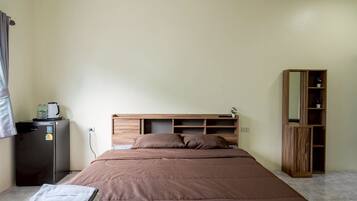 Ein Schlafzimmer mit einem Bett, einem kleinen Kühlschrank, einem Holzschrank und einem Spiegel.