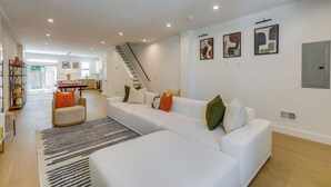 En moderne stue med et hvidt sofasæt, en stribet måtte og en trappe, der fører til et niveau oppe.