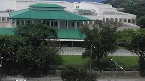 A large building with a green roof, surrounded by trees and a fence. - Grand Riviera neas Slec (Manila)