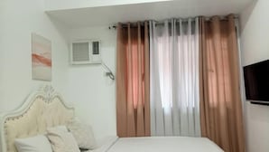 A bedroom with a bed, a headboard, a wall-mounted air conditioner, a window with curtains, and a flat-screen TV. - Grand Riviera neas Slec (Manila)