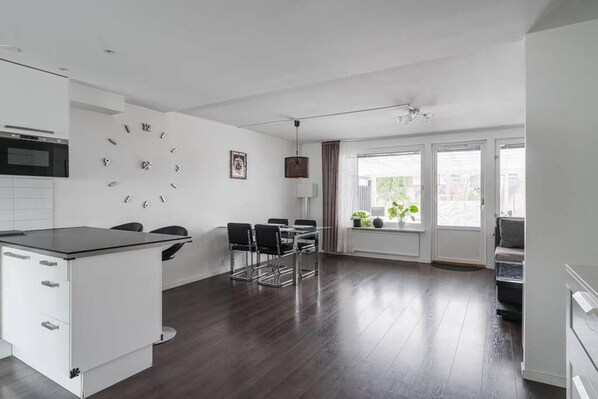 Une cuisine moderne avec une horloge, un coin repas avec des chaises et de grandes fenêtres.