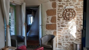 Quarto com paredes de pedra, um relógio de madeira, duas poltronas de couro, uma mesa pequena e uma escadaria que leva a outro espaço.