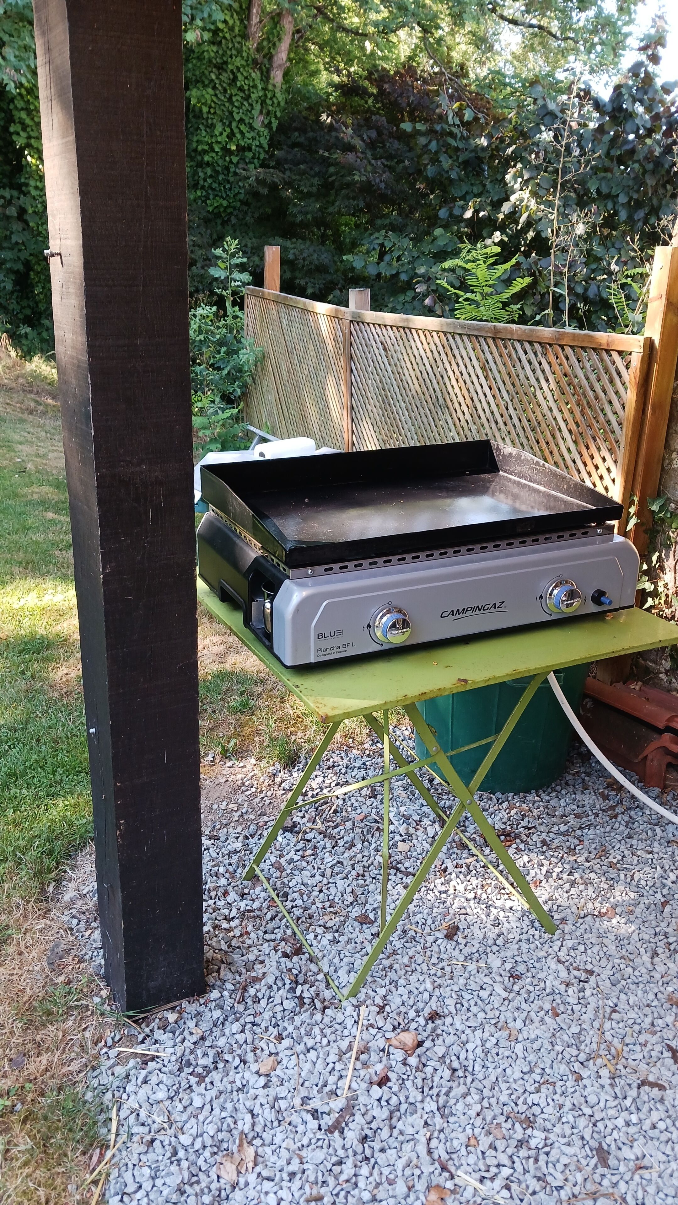 A portable camping stove on a green table with a wooden fence in the background.