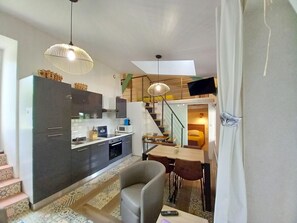 Un espacio habitable compacto con kitchenette, comedor y una escalera que lleva a un dormitorio.