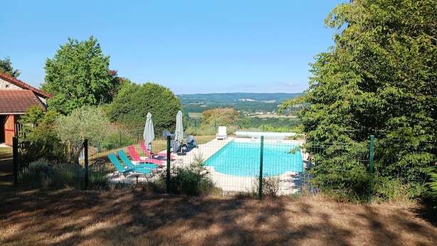 Piscina com espreguiçadeiras e guarda-sóis, rodeada por árvores e vista para o campo.