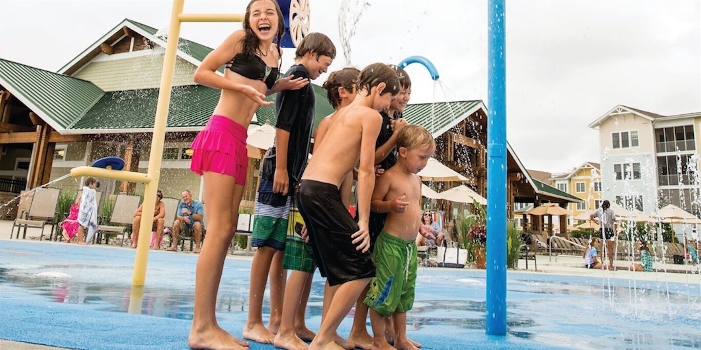 Een waterpark met een speelconstructie, een zwembad en gebouwen op de achtergrond.