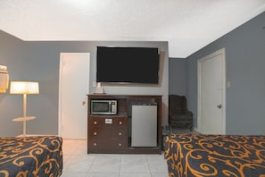 Habitación de hotel con dos camas, televisión, microondas, refrigerador, una silla y una lámpara.