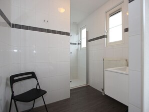 Een badkamer met witte tegels, een zwarte stoel, een douche en een raam.
