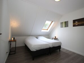 Een slaapkamer met een schuine kap, dakraam, een bed, nachtkastjes en wanddecoratie.