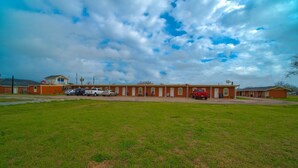 A building with a parking lot and a grassy field in front. - 3 Queen Beds|Smoking (Houston)