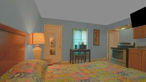 A bedroom with a bed, a desk, a chair, a television, and a kitchenette. - 3 Queen Beds|Smoking (Houston)
