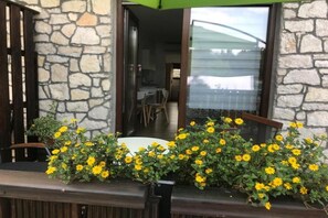 Eine Mauer aus Naturstein, eine Holzterrasse und gelbe Blumen.