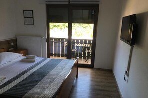 Ein Schlafzimmer mit Bett, Heizkörper, Fernseher und einem Balkon mit Tisch und Stühlen.