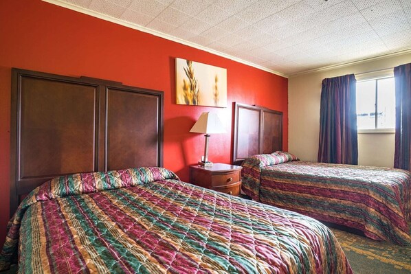 A hotel room with two beds, a nightstand, a lamp, and a window with curtains.