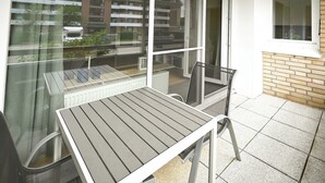 Ein Balkon mit Tisch und Stühlen, Blick auf ein Wohngebäude und ein Fenster mit Blick auf ein parkendes Auto.