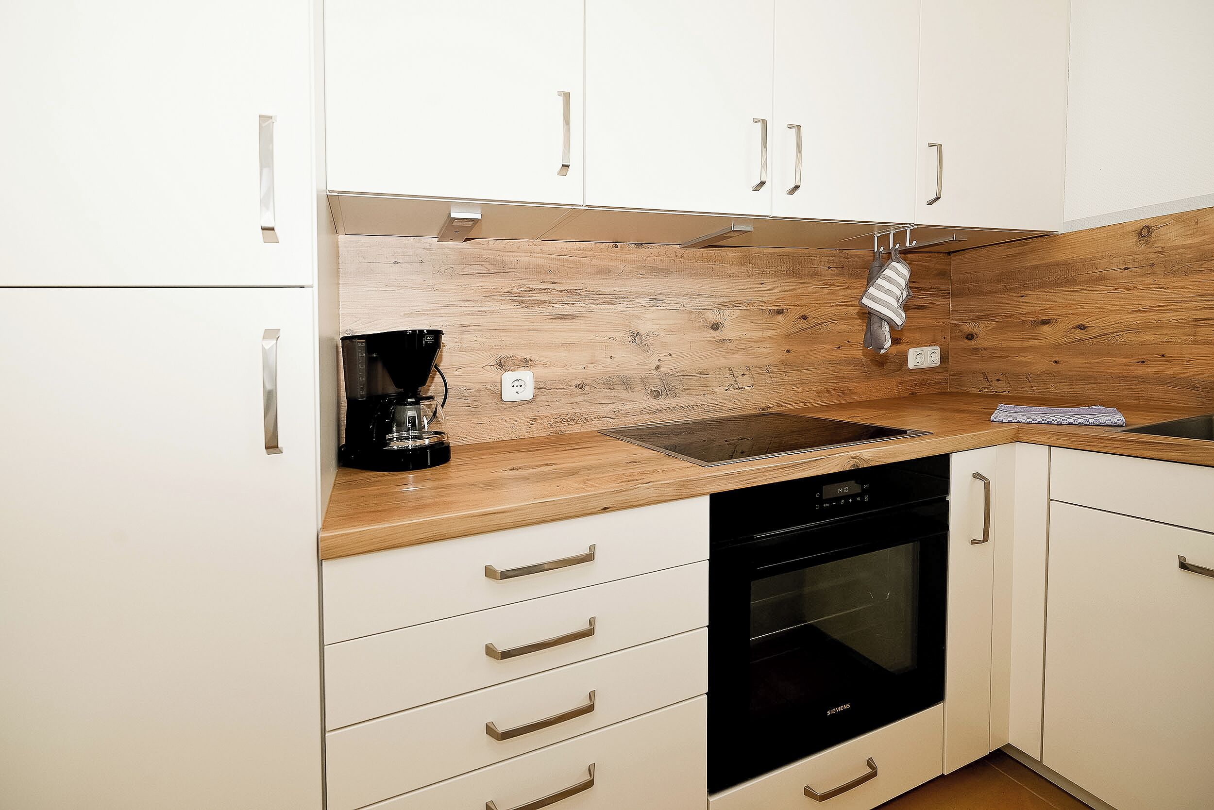 Eine Küche mit weißen Schränken, einer Holz Arbeitsplatte, einem schwarzen Geschirrspüler und einer Kaffeemaschine.