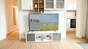 Ein modernes Wohnzimmer mit Flachbildfernseher, Holzregalen und einer Küche im Hintergrund.