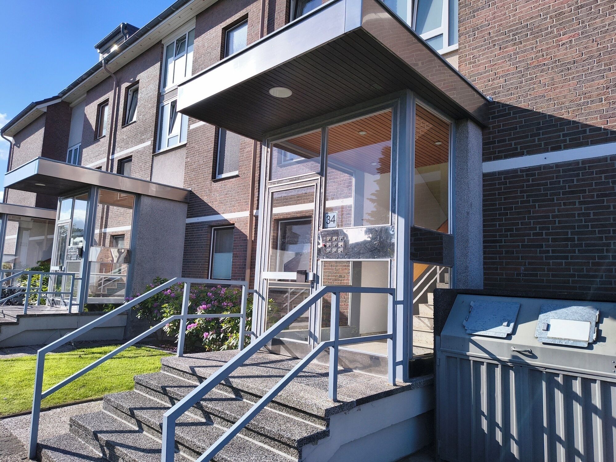 Un immeuble résidentiel à plusieurs étages, doté d’une façade en briques, de grandes fenêtres et d’un escalier menant à l’entrée.