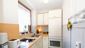 A compact kitchen with white cabinets, a built-in oven, a toaster, and a window with lace curtains. - Glück vacation apartment with balcony and lots of sunshine (Büsum)