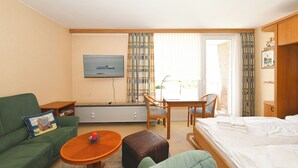 A hotel room with a bed, a green sofa, a wooden table, a TV, and a window with curtains. - Glück vacation apartment with balcony and lots of sunshine (Büsum)