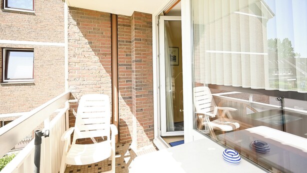 A balcony with white chairs, a glass door leading inside, and a view of the outside. - Glück vacation apartment with balcony and lots of sunshine (Büsum)