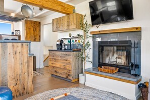 A modern kitchen with wooden cabinets, a built-in stove, and a television mounted above the fireplace. - Surf Inn - Monterey Beach House - Steps to the Beach! (Monterey)
