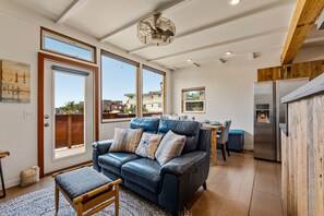 A modern living room with a leather sofa, a dining area, and a kitchen with a stainless steel refrigerator. - Surf Inn - Monterey Beach House - Steps to the Beach! (Monterey)