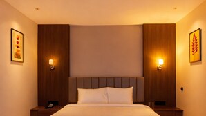 Habitación de hotel con una cama grande, cabecera de madera, lámparas de noche y cuadros en las paredes.