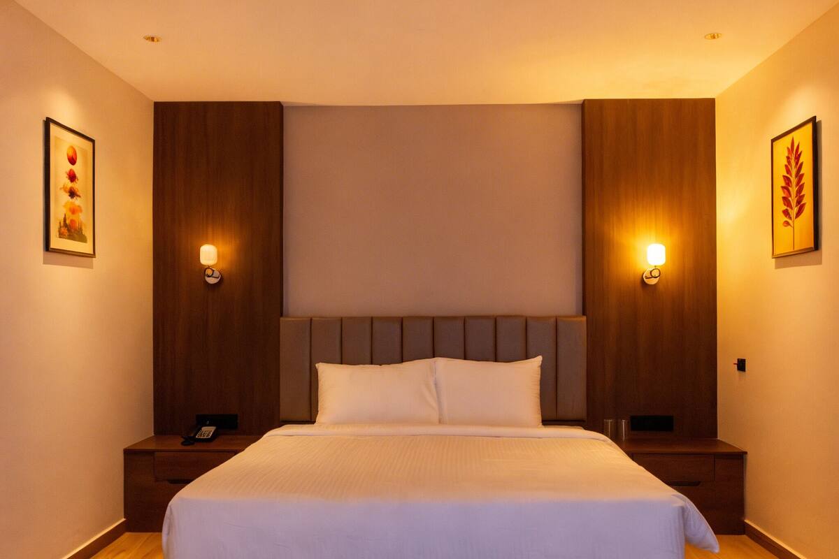 Une chambre d’hôtel avec un grand lit, une tête de lit en bois, des lampes de chevet et des œuvres d’art encadrées accrochées aux murs.