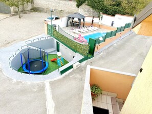 Ein Poolbereich auf dem Dach mit Trampolin, Liegestühlen und einer kleinen Spielzone.