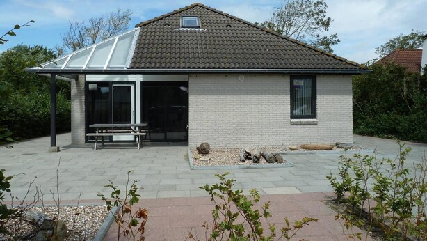 A single-story house with a tiled roof, a covered patio area, and a small garden.