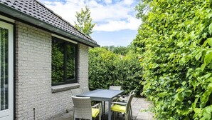 A patio with a table and chairs, a brick wall, and a hedge.