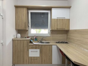A compact kitchen with wooden cabinets, a window with blinds, a sink, and a stove. - Studio Apartment Vir 2 (Vir)