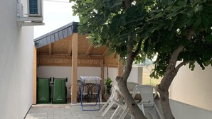 Espaço ao ar livre coberto com uma árvore, móveis de jardim e um contentor de lixo.