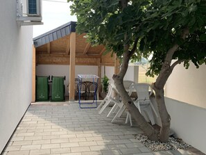 A covered outdoor area with a tree, outdoor furniture, and a trash bin. - Studio Apartment Vir 2 (Vir)