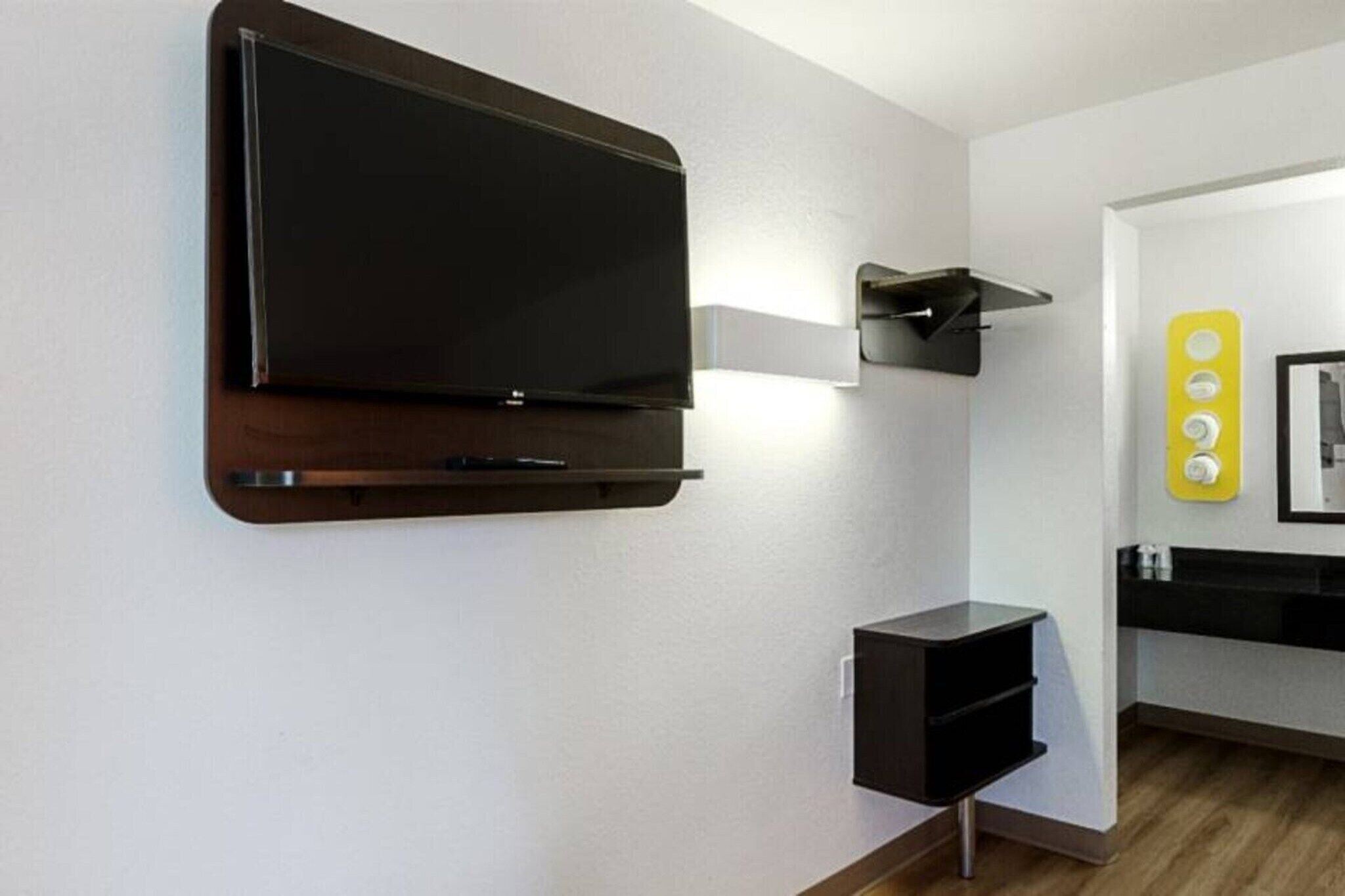 A modern room with a mounted TV, a small black cabinet, and a yellow light fixture.