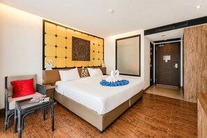 Ein Hotelzimmer mit einem großen Bett, einem Sessel, einem kleinen Tisch, einem Wandbild und einer Tür.