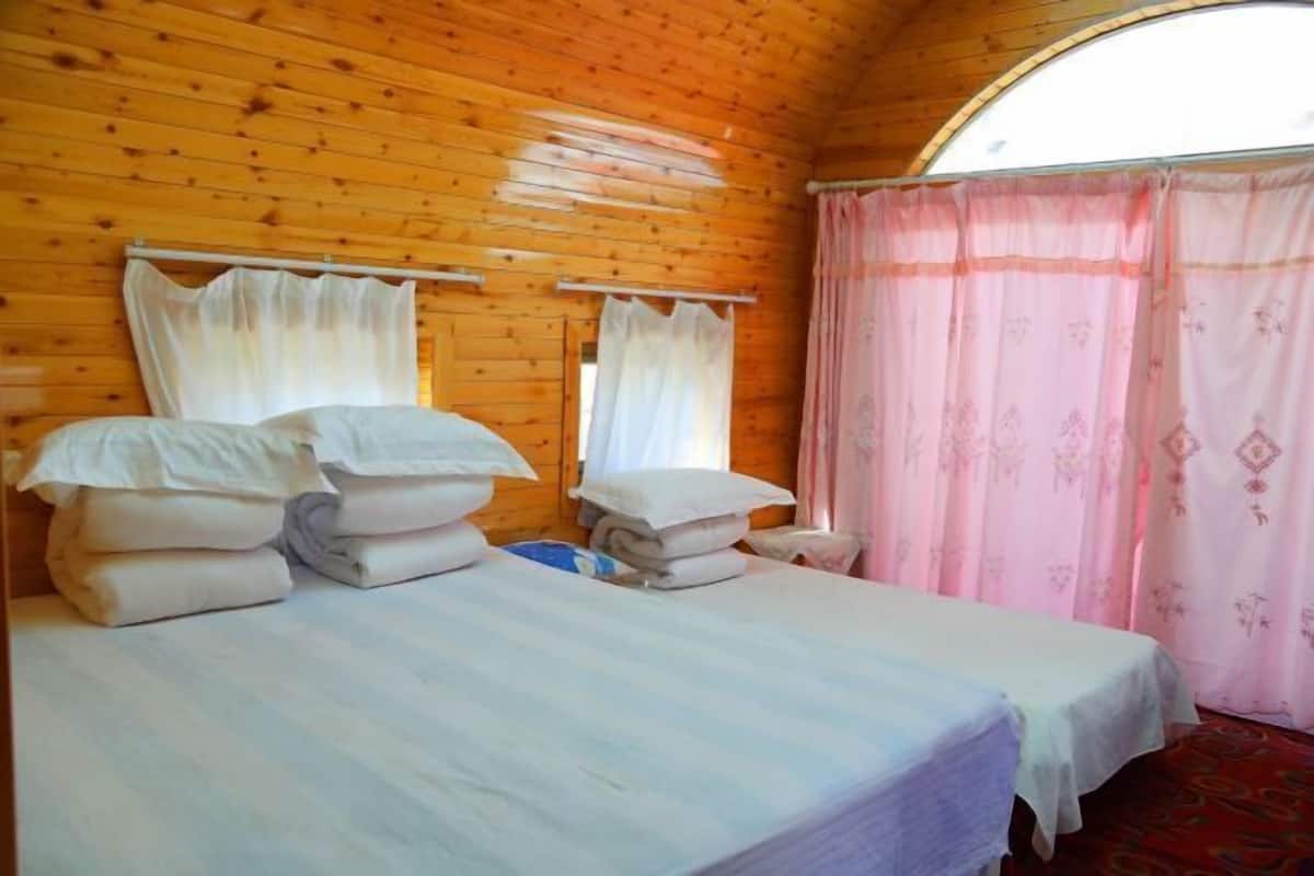 Habitación tipo cabaña de madera con dos camas, ropa de cama blanca y una ventana con cortinas.