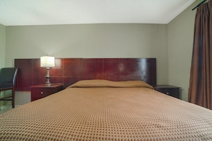 A hotel room with a bed, a nightstand with a lamp, a chair, and a wooden headboard.