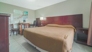 Et hotelværelse med en seng, et skrivebord, en stol, en lampe og et billede på væggen.