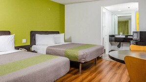 A hotel room with two beds, a small table, and a bathroom visible through an open door.